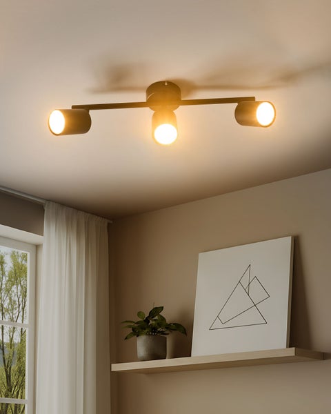 Dreiflammiger Deckenstrahler aus schwarzem Metall über einem Regal mit Dekoration und Vorhang im modernen Wohnzimmer.