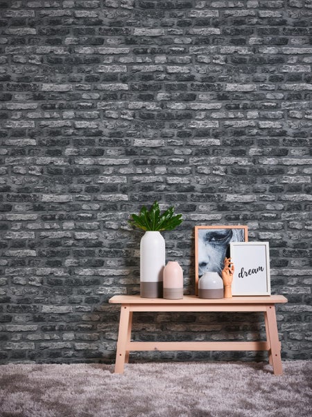 Arbeitszimmer mit Schreibtisch, Stuhl, Lampe und Dekoration vor einer Backsteinmauer
