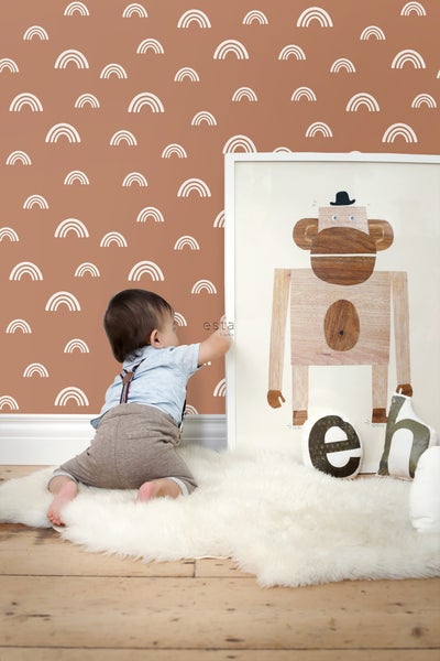 Zimmerszene mit Baby auf einem Schaffellteppich vor einer Wand mit Regenbogenmuster und einem gerahmten Bild eines Holzaffen.