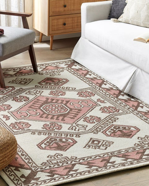 Teppich mit geometrischem Muster in einem hellen Wohnzimmer mit weißem Sofa, Holzkommode und grauem Sessel.