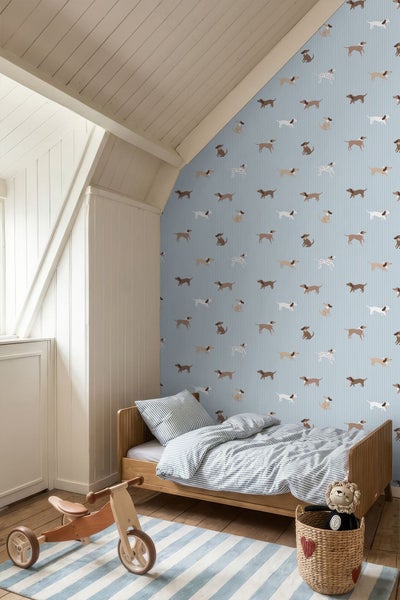 Helles Kinderzimmer mit gemusterter Hundetapete auf blauem Hintergrund, einem Holzbett und einem hölzernen Laufrad.