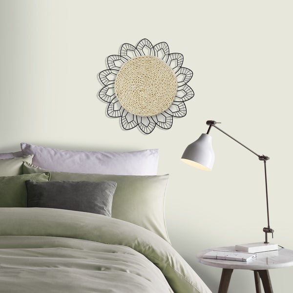 Runde Wanddekoration mit geflochtener Mitte und schwarzem Metalldekor, über einem Bett in einem hellen, modern eingerichteten Schlafzimmer.