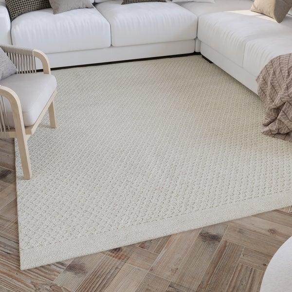 Hell eingerichtetes Wohnzimmer mit einem strukturierten In- und Outdoor-Teppich auf Holzfußboden, einem Sofa und einem Sessel.