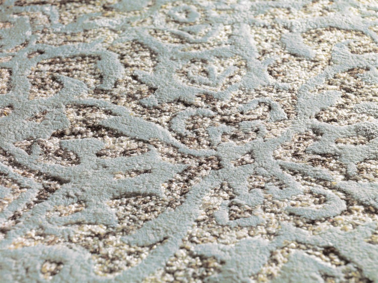 Nahaufnahme eines Teppichs mit einem reliefartigen, ornamentalen Muster und unterschiedlichen Texturen.