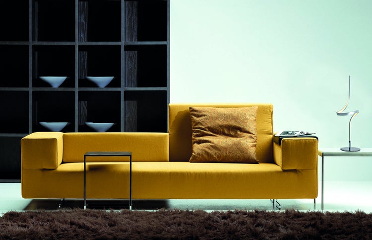 Wohnzimmer mit gelbem Sofa, Couchtisch, Bücherregal und Teppich für eine gemütliche Atmosphäre