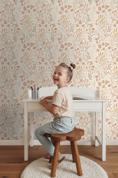 Ein Mädchen sitzt an einem weißen Schreibtisch vor einer Tapete mit Pflanzenmotiven.