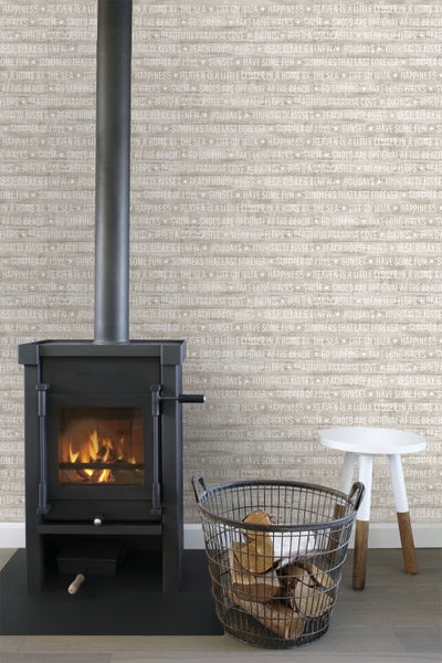 Szene mit einem schwarzen Kaminofen, einem Holzkorb mit Brennholz und einem weißen Hocker vor einer gemusterten Wand.