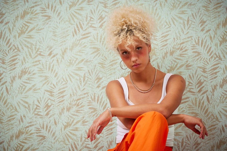 Frau mit Ohrringen und Halskette vor Tapete mit Blattmuster