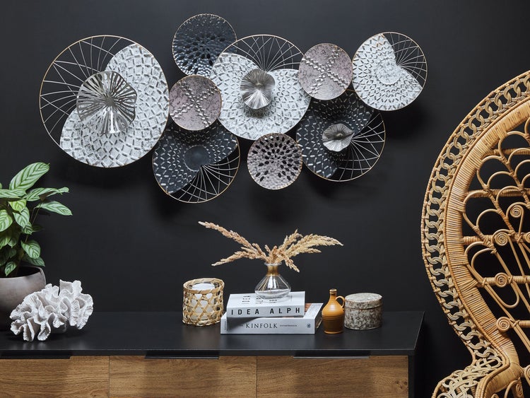 Dekoratives Wandobjekt aus Metall in verschiedenen Designs über einer Kommode mit Dekoration und einem Rattan-Sessel