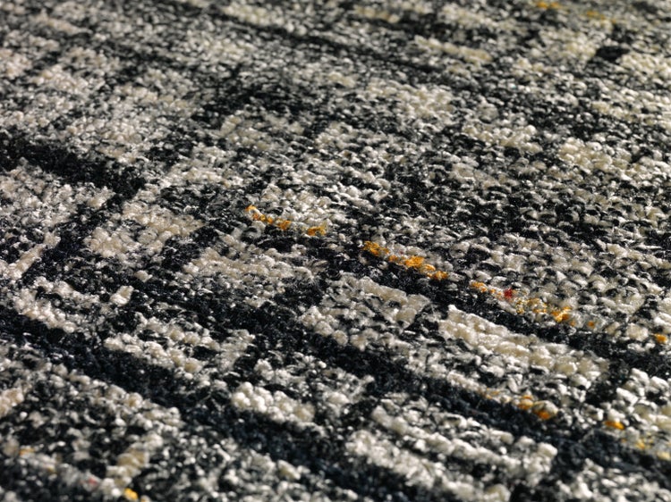 Nahaufnahme eines gewebten Teppichs mit abstraktem geometrischem Muster und sichtbarer Faserstruktur.