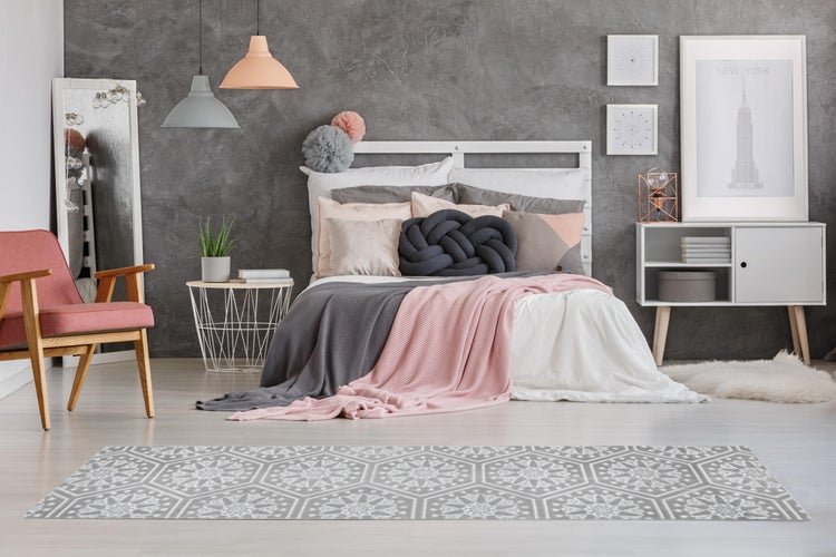 Modernes Schlafzimmer mit weißem Bett, grauen und rosa Textilien, grauer Wand in Betonoptik und einem gemusterten Läufer im Vordergrund.