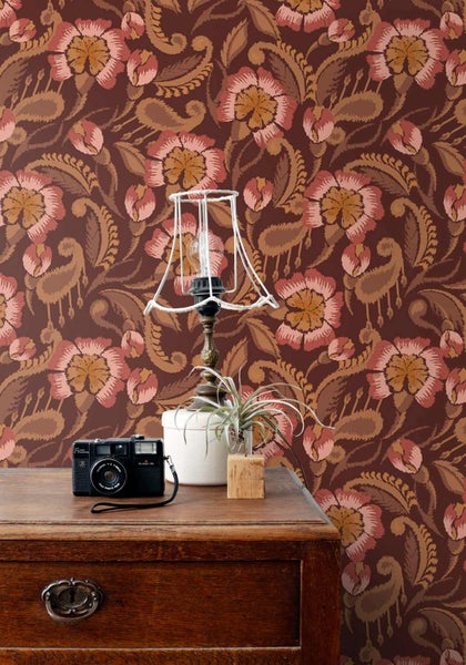 Vliestapete mit Blumenmuster und Paisley-Motiven an einer Wand hinter einer Kommode aus Holz mit Kamera und Lampe.