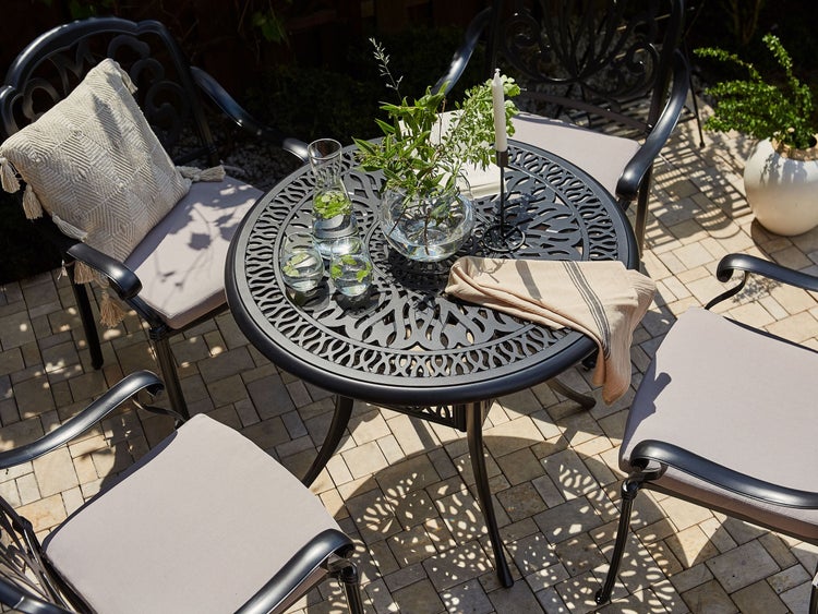 Gartensitzgruppe mit Tisch, Stühlen und Kissen auf einer Terrasse.
