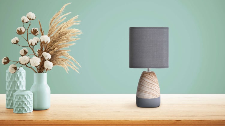 Dekorative Szene mit einer grauen Tischleuchte und Vasen mit Pflanzen auf einem Holztisch.