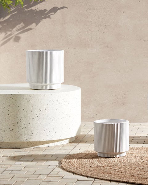 Zwei weiße Pflanzgefäße mit gerippter Oberfläche auf einer Terrasse