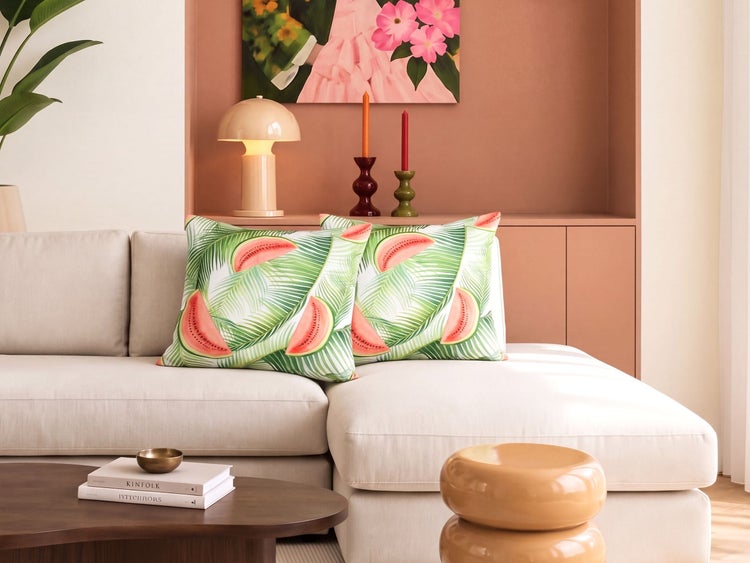Zwei quadratische Kissen mit Wassermelonen und Palmblattmuster auf einem hellen Sofa in einem modern eingerichteten Wohnzimmer.
