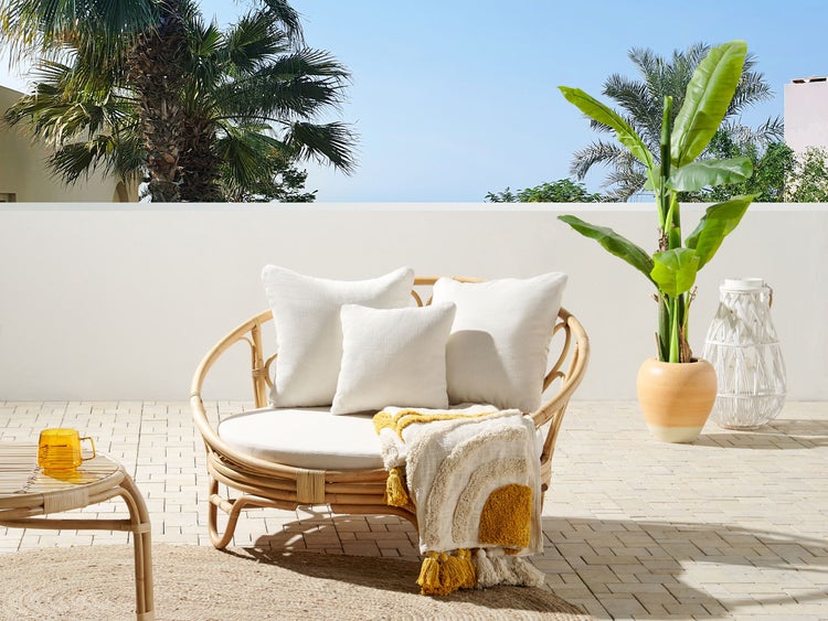 Szene mit Rattan-Sessel, Kissen, Decke, Beistelltisch und Pflanze für den Außenbereich.