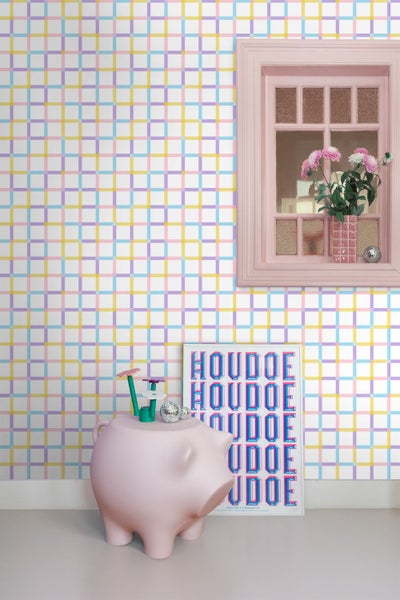 Wand mit karierter Tapete in Gelb, Blau, Lila und Rosa. Davor stehen ein rosa Hocker in Schweineform und ein Poster.