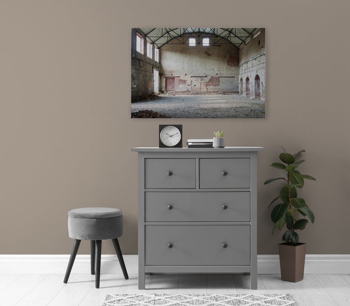 Wandbild mit Motiv einer leeren Industriehalle über einer grauen Kommode mit Hocker und Pflanze in einem modern eingerichteten Raum.