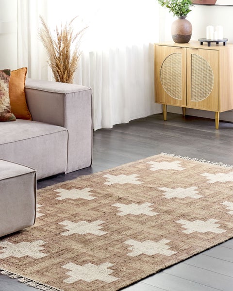 Helles Wohnzimmer mit braun-weiß gemustertem Teppich auf dunklem Boden, grauem Sofa und Sideboard aus Holz mit Geflechteinsätzen.