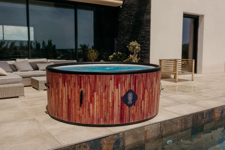 Aufblasbarer runder Whirlpool in Holzoptik mit COCO SPA Logo auf einer hellen, modernen Terrasse neben einem Swimmingpool.
