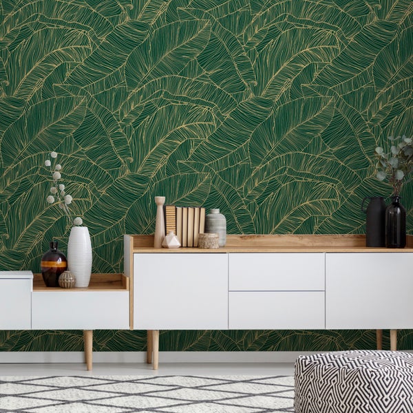 Vliestapete mit goldenem Blattmuster auf dunkelgrünem Hintergrund hinter einer modernen weißen Anrichte mit Holzdetails und Dekoration.
