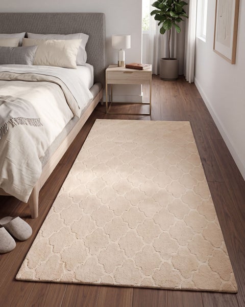 Beigefarbener Teppich mit geometrischem Muster vor einem Bett in einem modernen Schlafzimmer mit Holzboden.