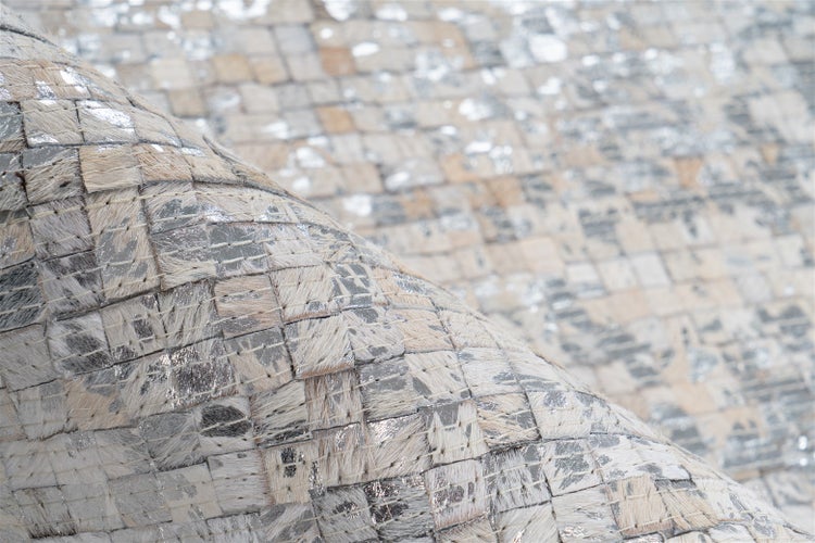 Detailansicht eines Kuhfellteppichs im Patchwork-Design mit natürlichen Fellstücken und silbernen Metallic-Akzenten.