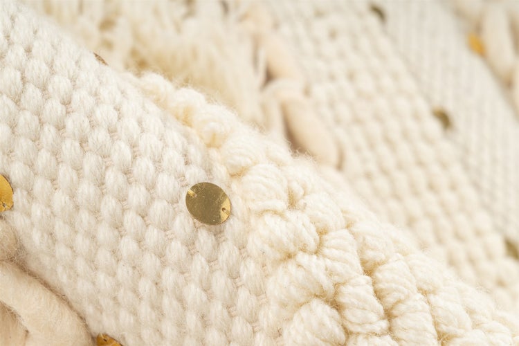 Nahaufnahme eines cremefarbenen, strukturierten Textils mit kleinen runden Goldpailletten.