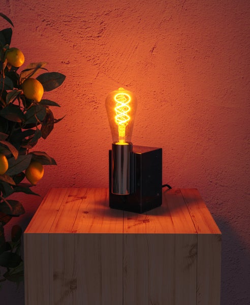 Dekorative Tischlampe mit Edison-Glühbirne auf einem Holztisch, neben einem Zitronenbaum