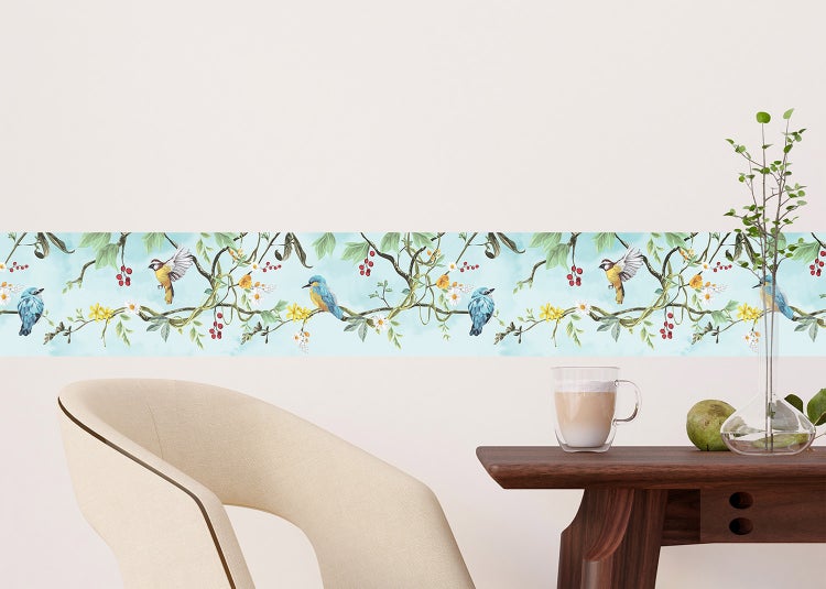 Tapetenbordüre mit Vogel- und Naturmotiv an einer Wand in einem hellen Raum mit Holztisch und Sessel.