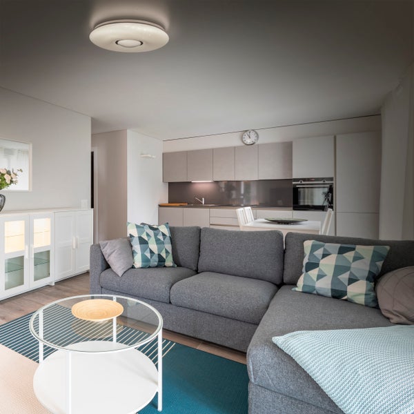 Helles Wohnzimmer mit grauem Sofa, Couchtisch aus Glas und Küchenzeile