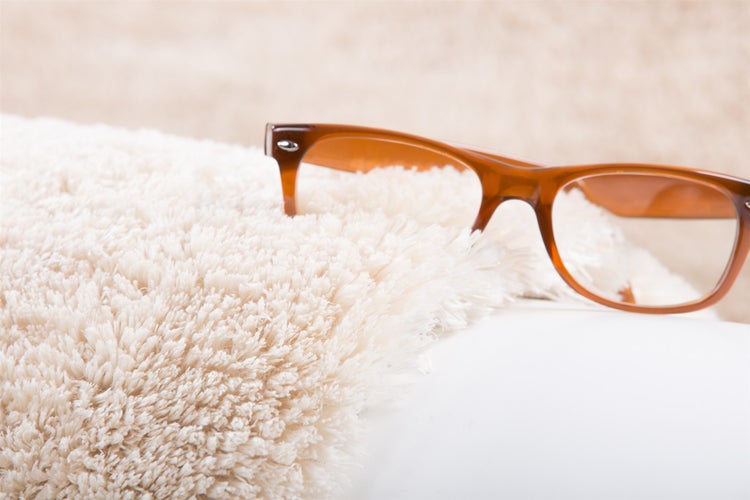 Nahaufnahme eines Hochflor Teppichs mit weicher Struktur und einer darauf liegenden Brille zur Veranschaulichung der Florhöhe.