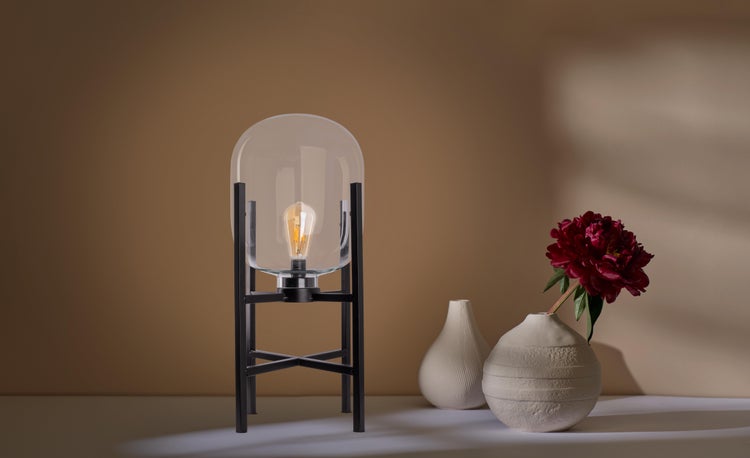 Dekorative Tischleuchte mit Glaskuppel und Metallgestell neben Vasen