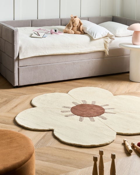 Blumenförmiger Teppich auf Holzparkettboden in einem hellen Kinderzimmer mit Polstersofa und Spielzeug.