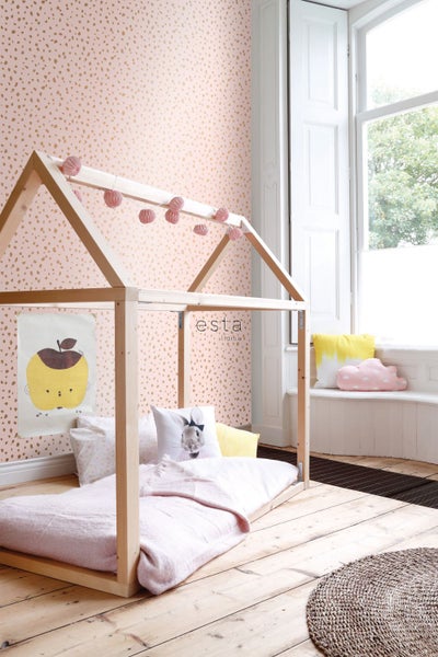 Helles Kinderzimmer mit einem Holzbettgestell, einer rosa Tapete mit Punktmuster und dekorativen Kissen