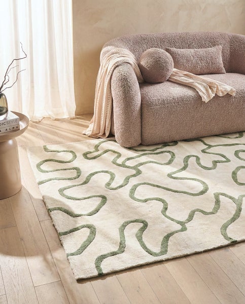 Moderner Teppich mit grünem Wellenmuster auf hellem Grund in einem hellen Wohnzimmer vor einem Sofa auf Holzboden.