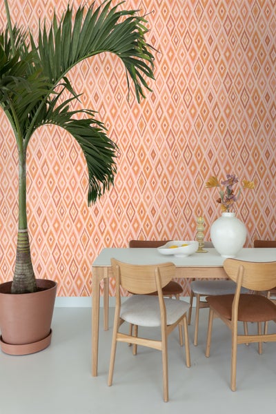 Innenaufnahme eines Esszimmers mit Esstisch, Stühlen und Zimmerpflanze vor einer gemusterten Tapete