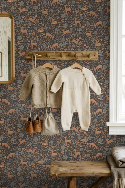 Kindertapete mit Waldmotiven und Rehen vor einer Wand mit hängender Kleidung und einer rustikalen Holzgarderobe in einem Kinderzimmer.