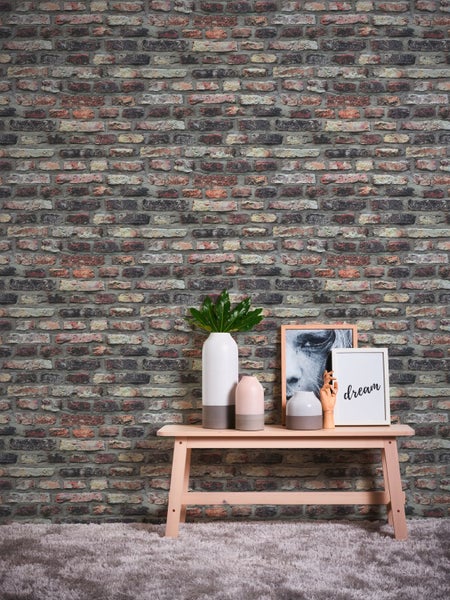 Nahaufnahme einer Wand mit Backsteintapete, einem Tisch, einer Zimmerpflanze, einem Deko-Haus und einem Bilderrahmen.