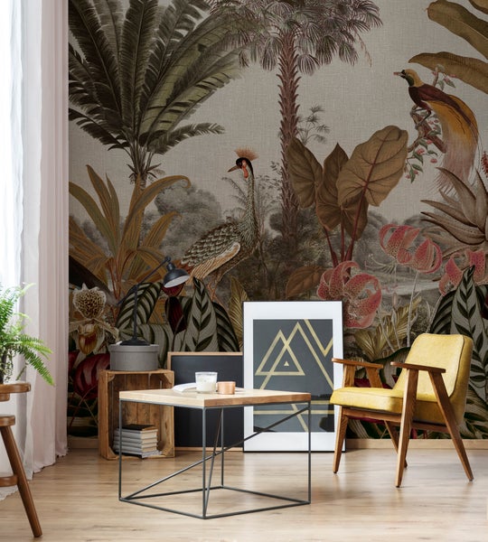 Wohnzimmer mit Vliestapete im Tropen Design mit Vögeln und Pflanzen, kombiniert mit einem Sessel und einem Beistelltisch aus Holz.