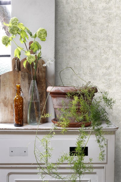 Gemusterte Tapete mit Blumen, Topfpflanze und Dekoration auf einer Kommode.