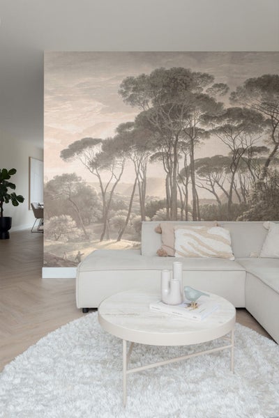 Helles Wohnzimmer mit großflächiger Fototapete einer Pinienlandschaft, einem Ecksofa, rundem Marmortisch und Hochflorteppich auf Fischgrätparkett.