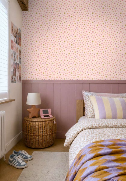 Ein Kinderzimmer mit Sternchentapete und holzverkleideter Wand, mit Bett, Korbtisch und Nachttischlampe in einem modern eingerichteten Raum.