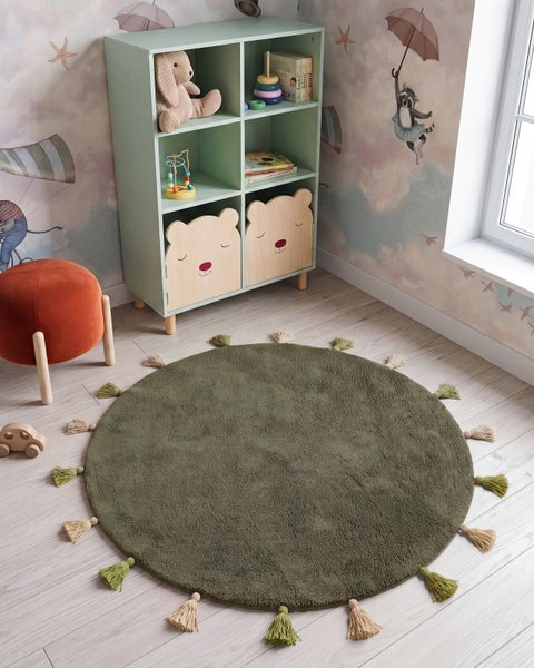 Runder Kinderteppich mit Quasten im Kinderzimmer mit Spielzeugregal und Hocker.