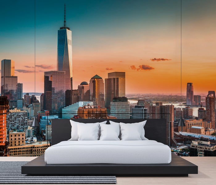Fototapete mit New York City Skyline bei Sonnenuntergang und One World Trade Center, angebracht in einem Schlafzimmer hinter einem modernen Bett.