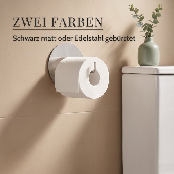 Wandmontierter Toilettenpapierhalter aus gebürstetem Edelstahl, montiert an einer Fliesenwand neben einem WC mit Pflanzendekoration.