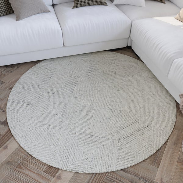 Runder Teppich mit strukturiertem, geometrischem Muster aus Quadraten, platziert vor einem Sofa auf einem Holzfußboden.