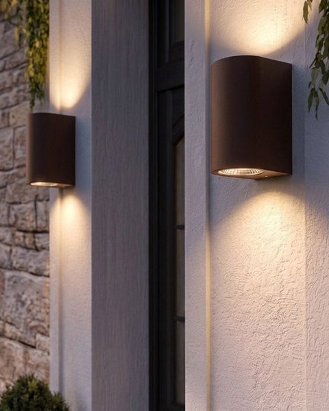 Zwei moderne zylindrische Außenwandleuchten mit Lichtkegel nach oben und unten an einer strukturierten Hausfassade.