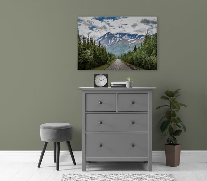 Wandbild mit Berglandschaft und Eisenbahngleis über einer grauen Kommode in einem modern eingerichteten Raum.